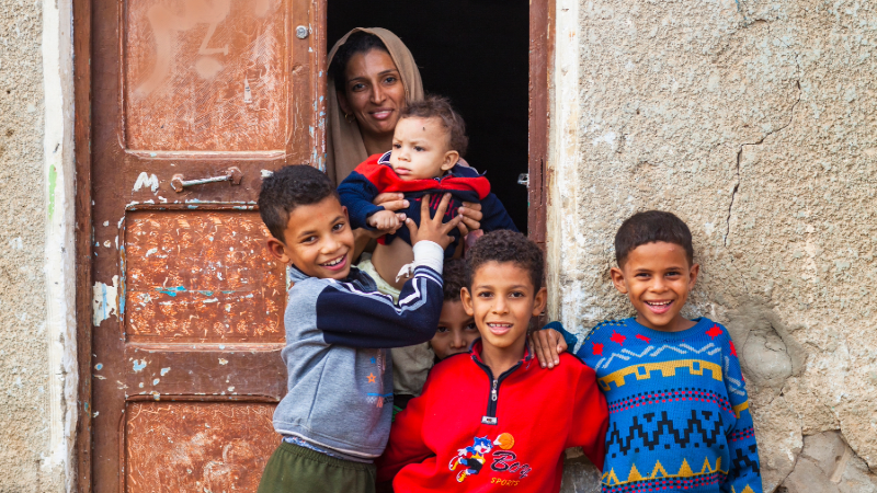 a woman and her four children dressed in red and blue jumpers stand at the door to their home