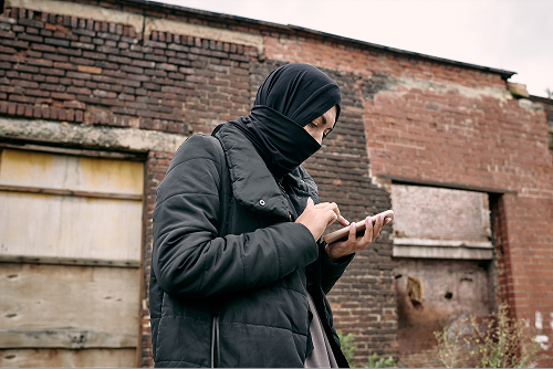 a woman in head covering using her phone with run down brick background